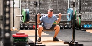 sportsman doing back squat exercise with barbell in gym