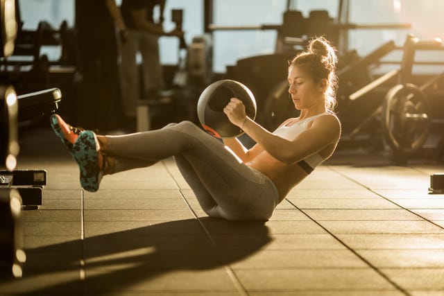 Sportswoman doing sit-ups with medicine ball on sports training in a gym.