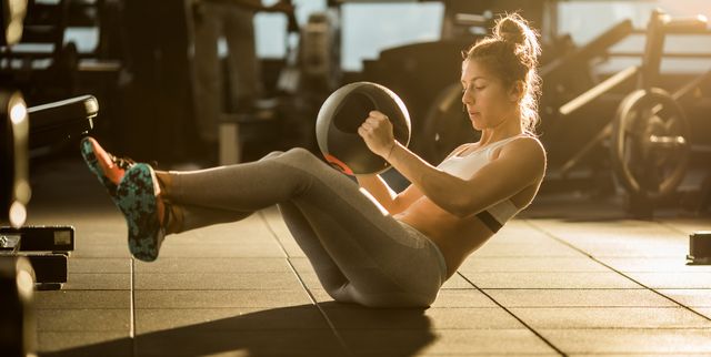 Sportswoman doing sit-ups with medicine ball on sports training in a gym.