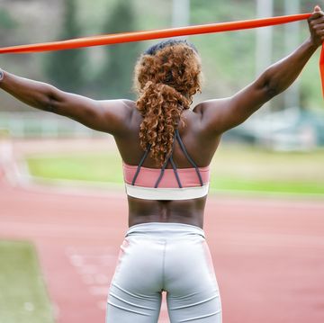 sportswoman stretching resistance band while standing on running track
