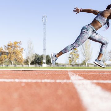 sportswoman with dedication running on sports track against clear sky during sunny day