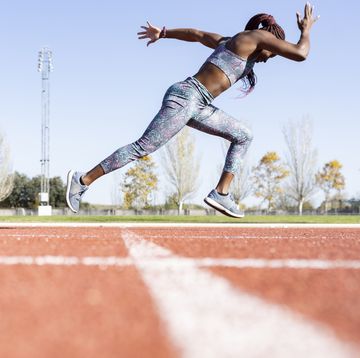 sportswoman with dedication running on sports track against clear sky during sunny day