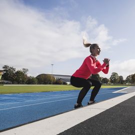 sportswoman with wireless headphones doing jumping exercise on track