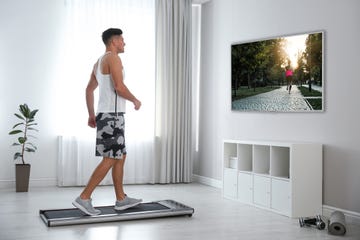 sporty man training on walking treadmill and watching tv at home