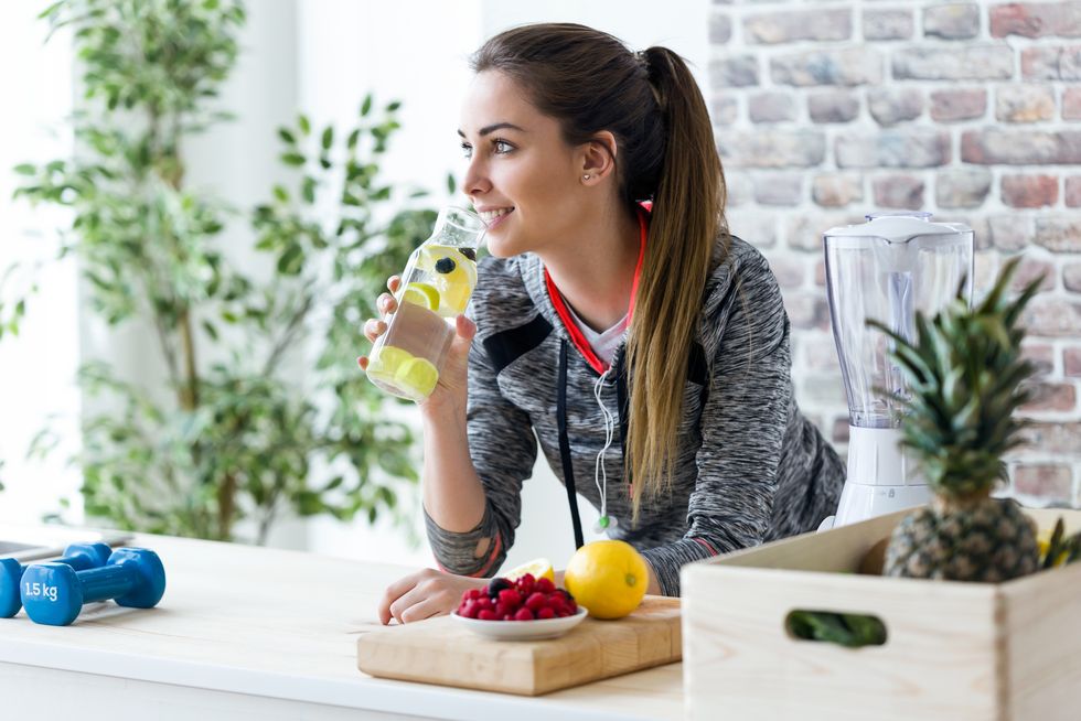 sporty young woman looking sideways while drinking lemon juice in the kitchen at home