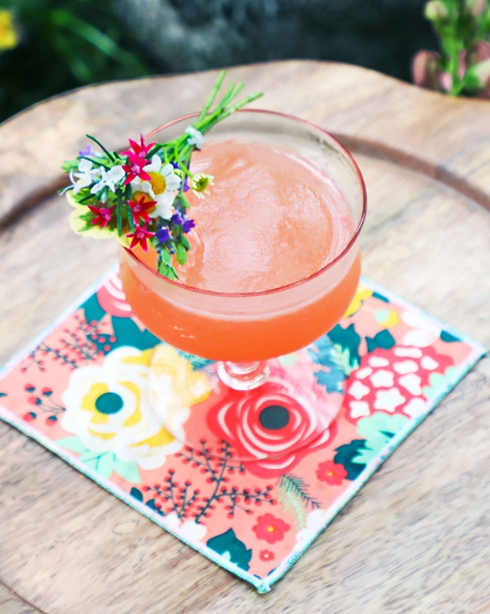pink cocktails spring bouquet served in a coupe with tiny bouquet of flowers as garnish placed on a colorful floral coaster