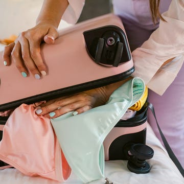 woman with pastel colored nail polish stuffing pink suitcase with swimsuit and clothes