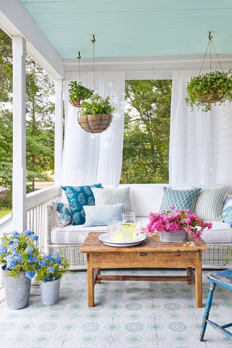front porch with white sofa decorated with blue and white patterned pillows, there are also many spring plants dotted around