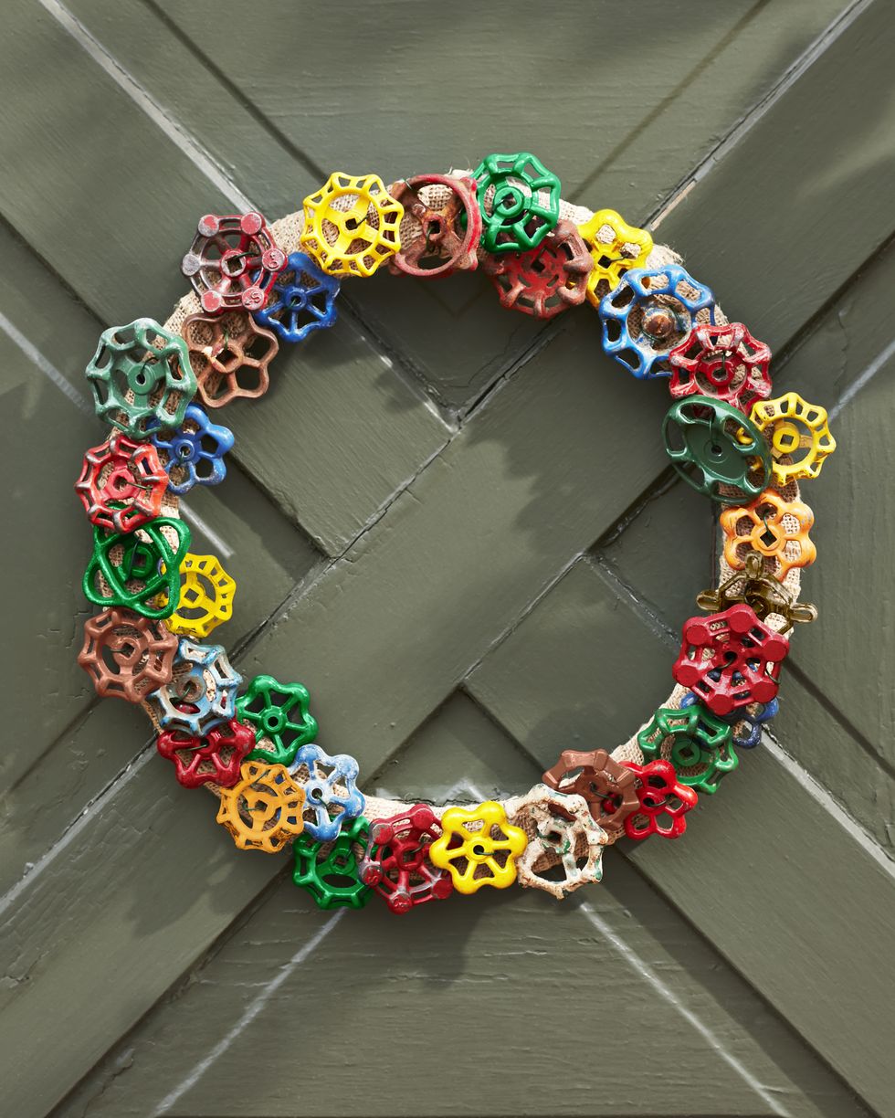 a wreath made from colorful vintage faucet handles hung on a olive green door