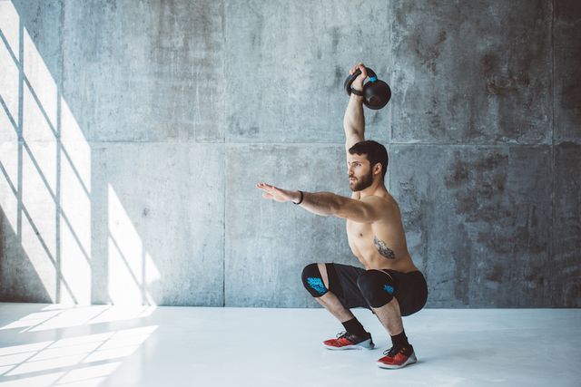 male fitness athlete performing overhead squat with kettlebell