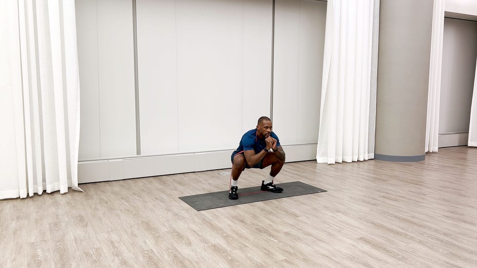 man performing a squat exercise on a mat with a resistance band in a gymlike environment