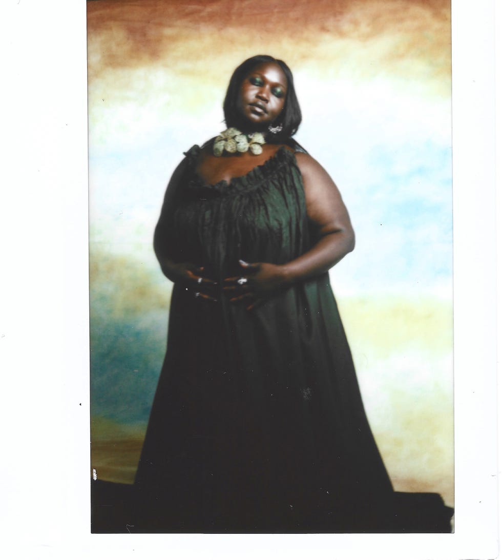 a figure stands against a softly colored background, dressed in a flowing dark gown