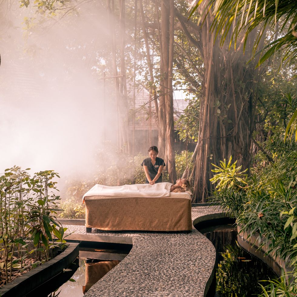 a person sitting on a stone bench in a forest the spa by thalgo france at ﻿sun siyam iru fushi