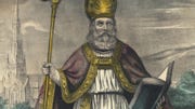a drawing of saint patrick wearing white robes, a red cap with gold trim, and a gold pointed hat, he is holding a gold staff in one hand and an open book in the other while looking upward toward the sky