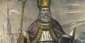 a drawing of saint patrick wearing white robes, a red cap with gold trim, and a gold pointed hat, he is holding a gold staff in one hand and an open book in the other while looking upward toward the sky