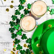two glasses of bear with green hot four leaf clover necklaces gold coins rainbows on white wood table st patricks day instagram captions