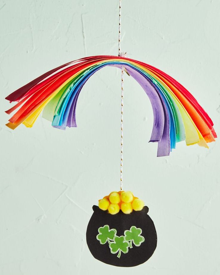st patricks day mobile craft with paper strips rainbow suspended above black paper pot filled with yellow mini pompoms