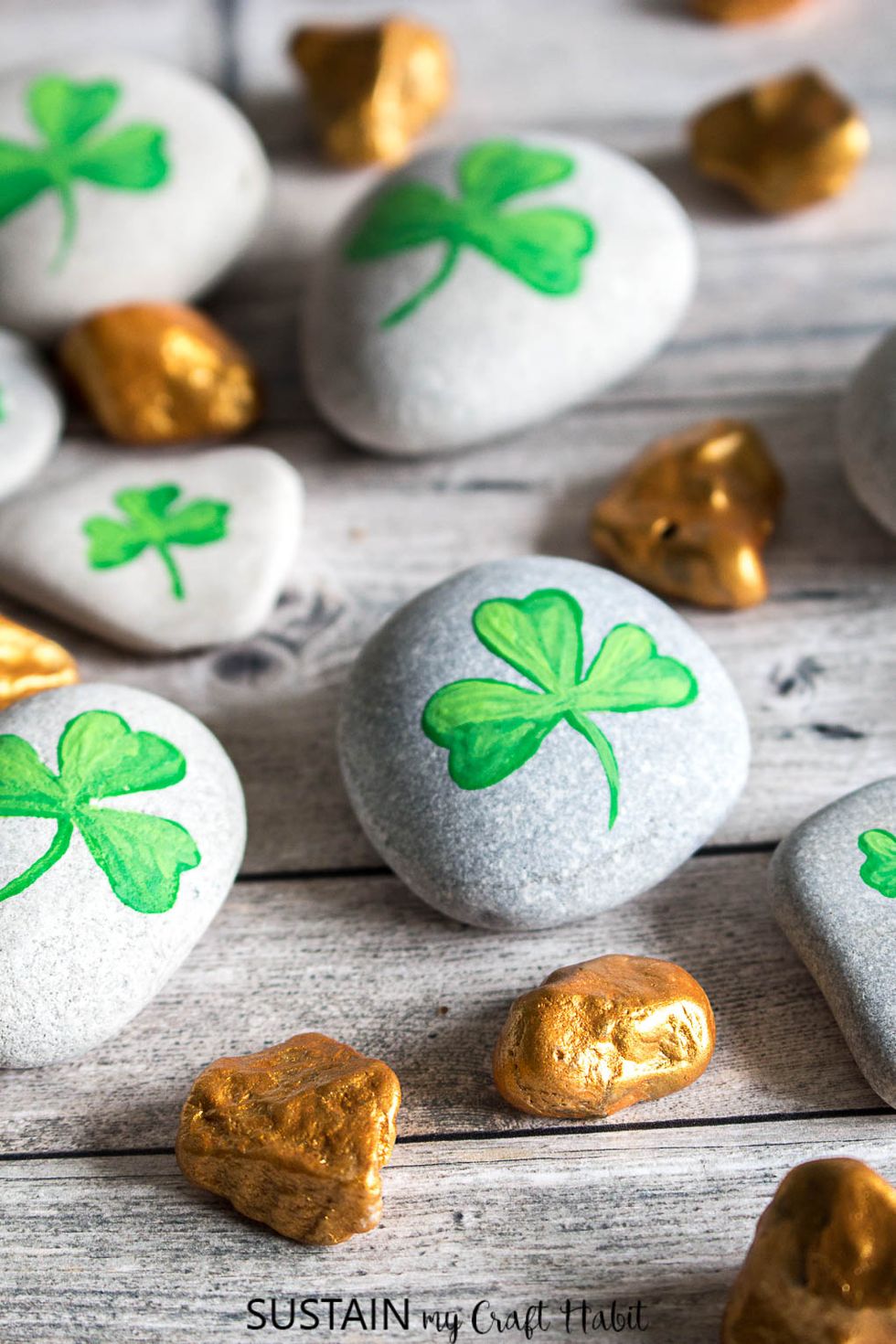 green shamrocks painted on smooth white rocks scattered among smaller rocks painted gold for an easy st patrick's day craft