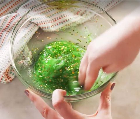 hands mixing green slime flecked with gold glitter for saint patrick's day