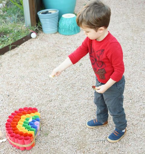 preschool child trying to toss gold coins into colorful short paper tubes arranged in rainbow shape for a st patricks day game
