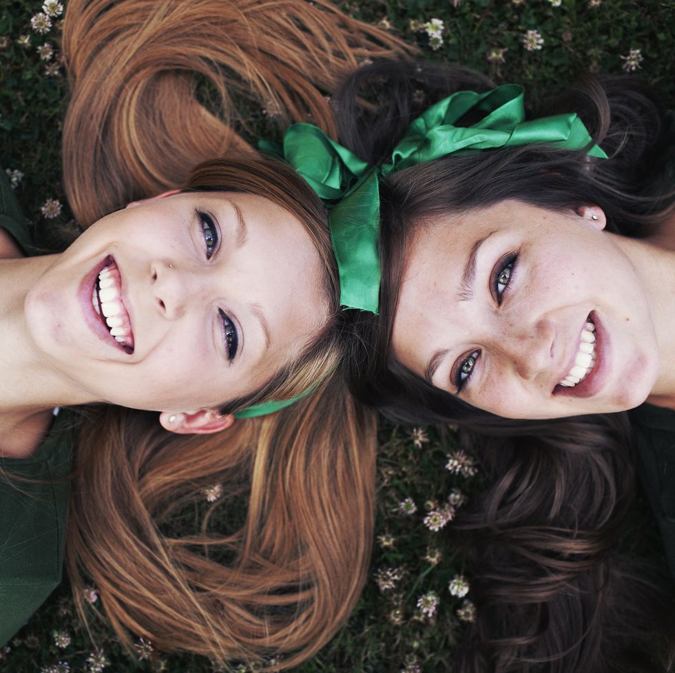 two girls laying down on the grass laughing upwards towards the sky it might be st patricks day because of the green bows in their hair