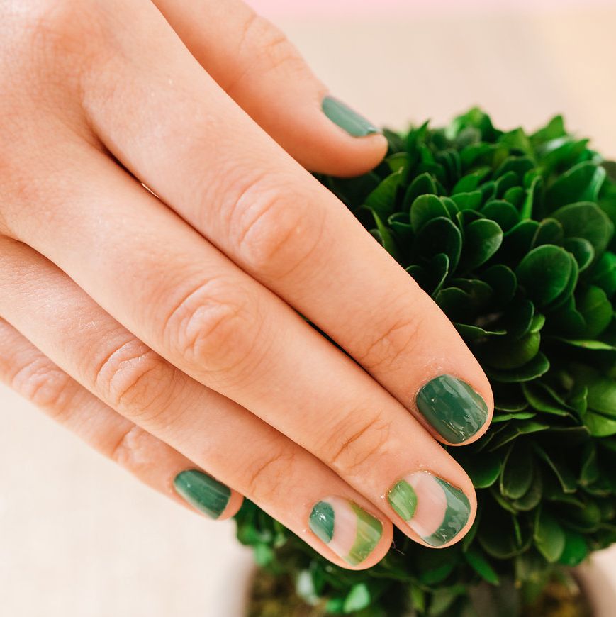 a female hand with green nail polish and a green plant in the background