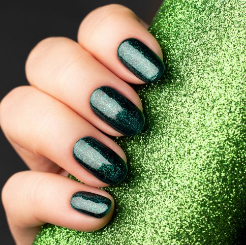 female hand with beautiful holiday manicure green glittered nails with glitter paper background