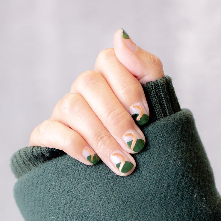 a woman's hand closed over her sweater with nails painted with green polish and a gold squiggle