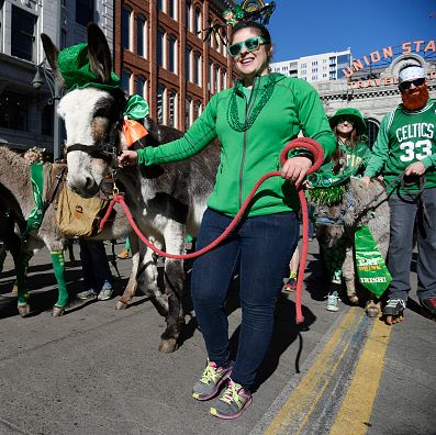 people dressed in green leading burros in green hats down the street in front of union station on a sunny day