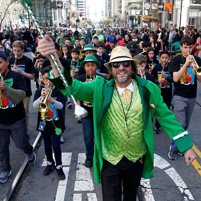 musicians march and perform with a band leader dressed in a straw fedora, green suit, light green vest and sunglasses leading them