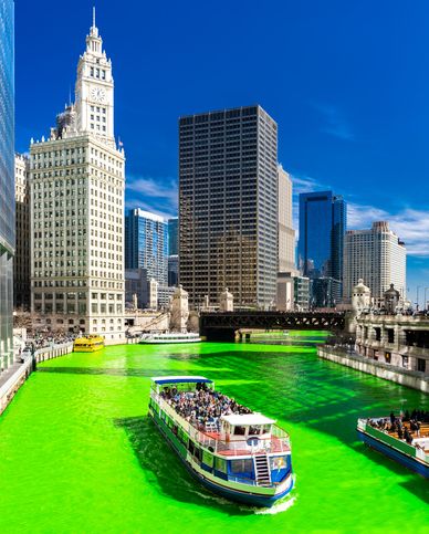 chicago river dyed green with skyscrapers around it and a tour boat on the water