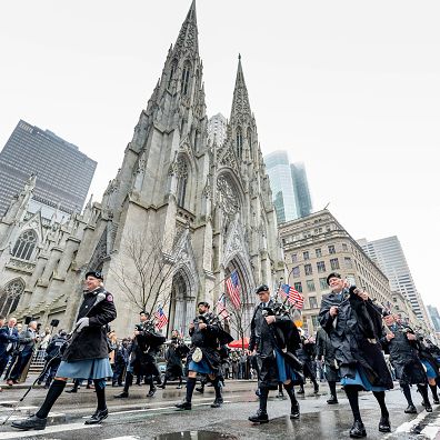 police officers playing bagpipes in traditional dress march across st patricks cathedral during nyc st patricks day parade