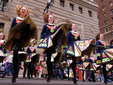 irish dancers with curly red hair and navy blue skirts with celtic symbols step dancing during st patricks day parade