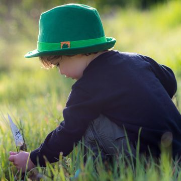 young boy playing in the grass wearing a green fedora hat for st patricks day