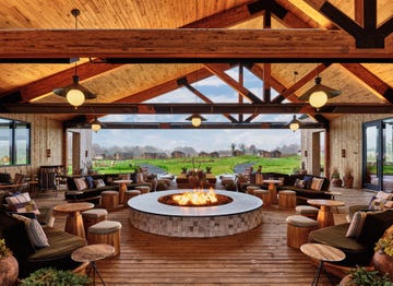 a spacious lounge area features a centrally located circular fire pit surrounded by various seating options, including low chairs and stools