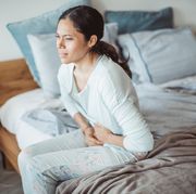 stabbing pain in stomach  woman sitting on bed holding her stomach