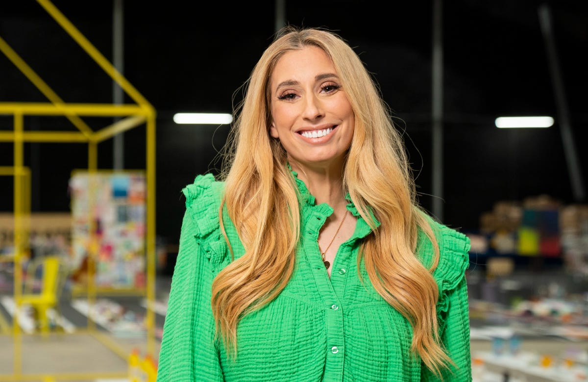 stacey solomon standing in a warehouse, smiling at the camera