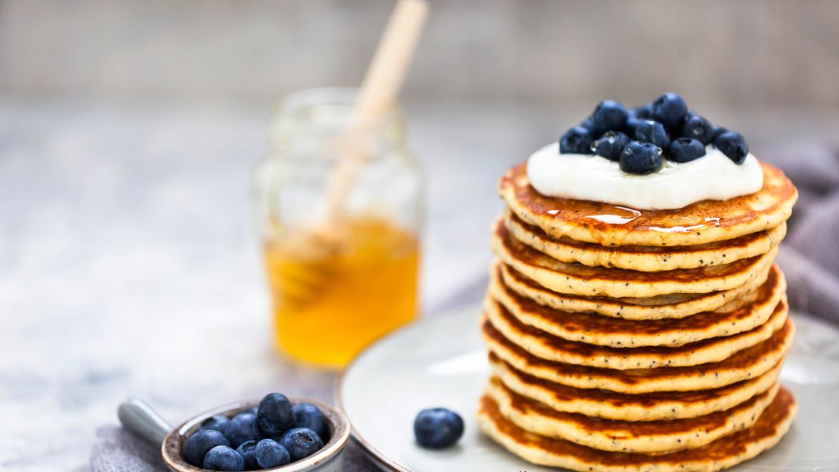 stack of freshly prepared lemon poppy seed pancakes topped with sour cream and blueberries