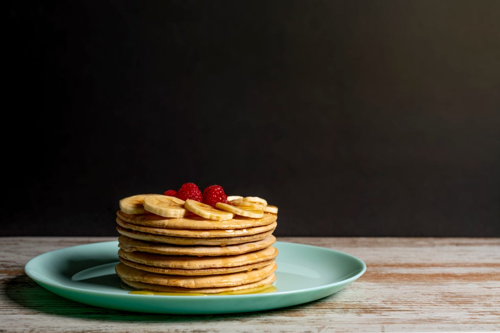 stack of pancakes with honey, bananas and raspberries