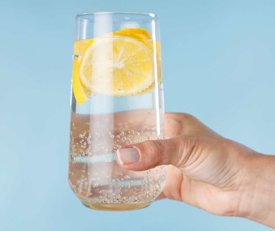 a hand holding a glass of sparkling water with lemon slices