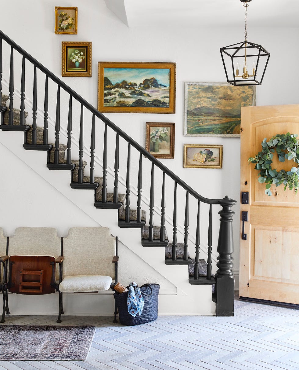 an entryway with black stair rails and vintage paintings