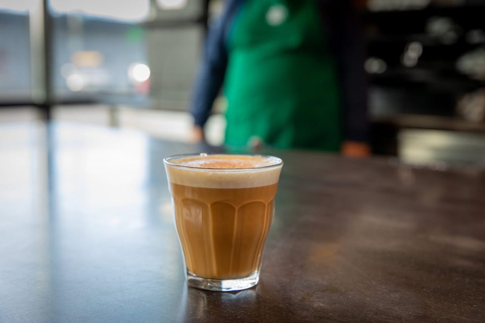 glass of brown latte on a table with a blurred barista in the background