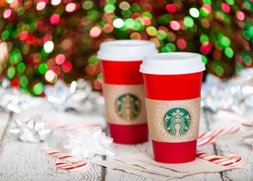 two red starbucks cups next to candy canes and silver bows in front of glittering lights