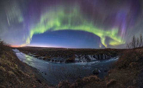 Een groenmetpaarse lichtshow van het Noorderlicht vult de nachthemel boven de watervallen van de rivier de Hvita op IJsland