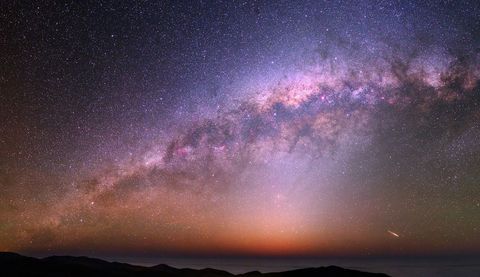 Tijdens een heldere nacht boven de Atacamawoestijn is in de kleurrijke nachthemel en onder een grandioze Melkweg de reflectie van een satelliet te zien