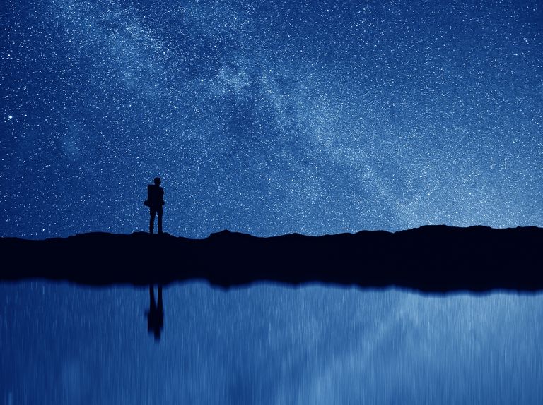 silhouette of a person standing outside near a body of water stargazing