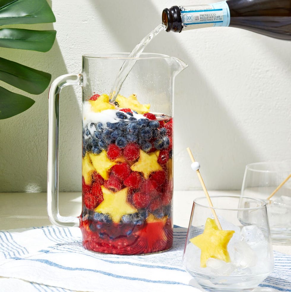 blueberries, raspberries, and star pineapples in a pitcher with prosecco