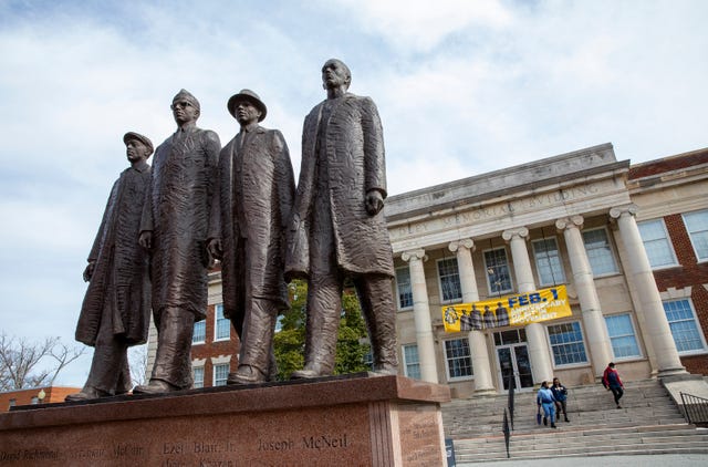 a statute of four men standing side by side in front of a college building