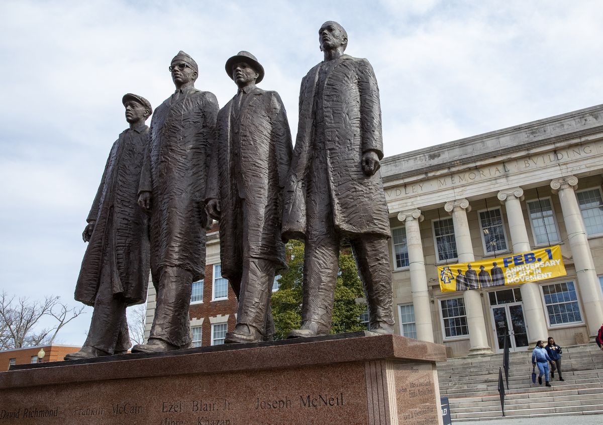 a statute of four men standing side by side in front of a college building