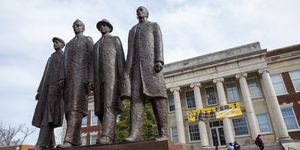 a statute of four men standing side by side in front of a college building